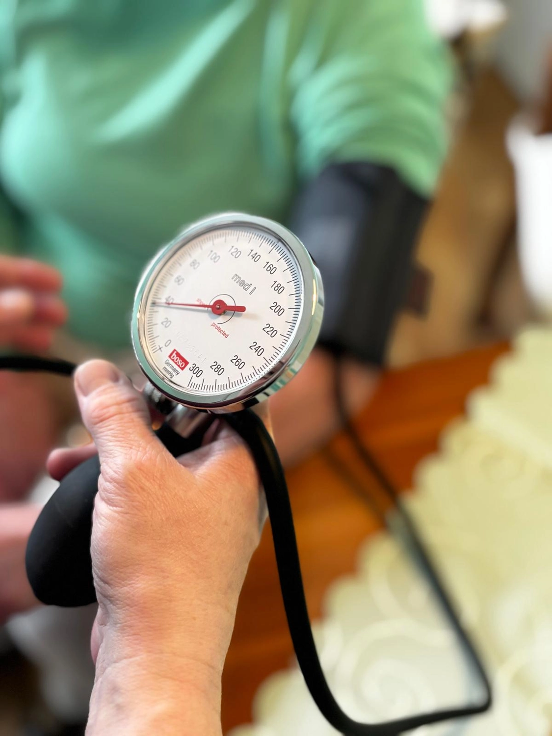 Pflegedienst Döring - Ambulanten Pflegedienstes - Nahaufnahme einer Hand, die ein manuelles Blutdruckmessgerät (Sphygmomanometer) mit rundem Zifferblatt und schwarzem Gummiballon hält.